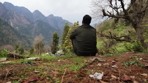 Man Sitting on a Hillside Overlooking a Scenic Himalayan Mountain Valley Stock Footage 344015367