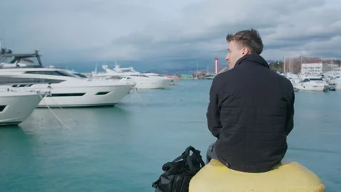 Man sitting with his back towards the camera and watching the sea and yachts Stock Footage 151077536