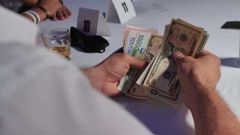 Man sitting with his back at white table counts money from different countries Video stock 104618744
