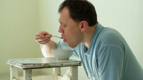 Man sitting on his lap in an empty room eating Chinese noodles, side view Stock Footage 132297887