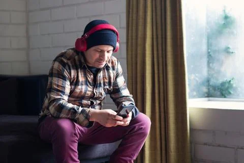 Man sitting at home checking his cell phone and listening to music Stock Photos