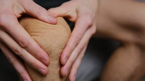 A man sitting at home giving his knee a massage after experiencing joint pain, f Stock Footage 296424924