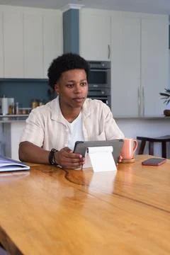 Man sitting at home kitchen table holding tablet on stand with orange mug, red Stock Photos
