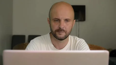 A man is sitting at home at a table and surfing the Internet at a laptop Vídeo Stock 145626917