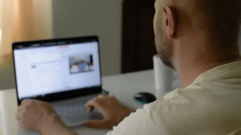 A man is sitting at home at a table and surfing the Internet at a laptop Vídeo Stock 145626946