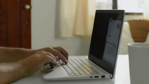 A man is sitting at home at a table and surfing the Internet at a laptop Vídeo Stock 145626972