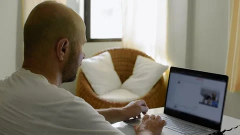 A man is sitting at home at a table and surfing the Internet at a laptop Video stock 145627159