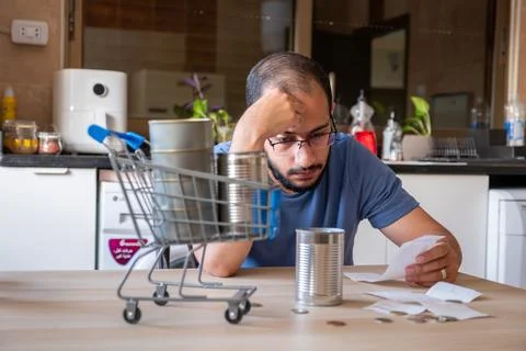 Man sitting in the kitchen holding receipt feeling frustrated due inflation.. Stock Photos
