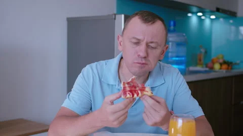 A man sitting at the kitchen table eating a slice of pizza with gusto Stock Footage 331121740