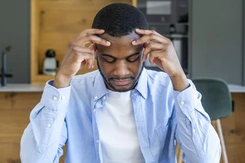 Man sitting at kitchen table with hands on temples, appearing stressed and .. Stock Photos