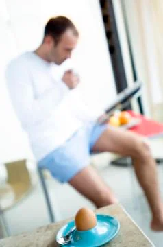 Man sitting on kitchen table, reading magazine, boiled egg in foreground Stock Photos