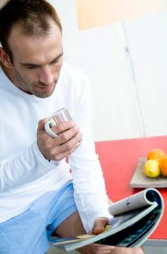 Man sitting on kitchen table, reading magazine, holding mug Stock Photos