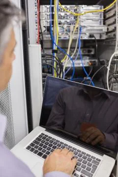 Man sitting with a laptop in front of a server Stock Photos