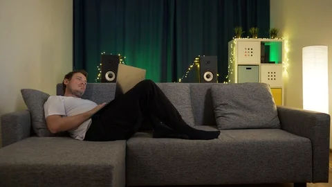 Man sitting with laptop on sofa and is typing a message Stock Footage 129384441
