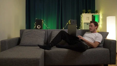 Man sitting with laptop on sofa and is typing a message Stock Footage 129384472