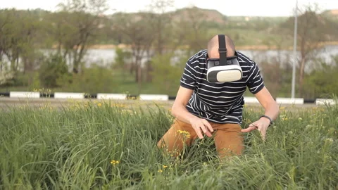 A man sitting on the lawn in a virtual reality helmet.Dive games or panoramic Stock Footage 92281318