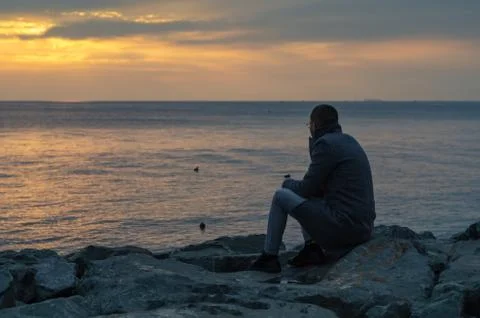 Man is  sitting on a ledge of a sea, Stock Photos