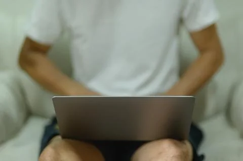Man sitting with legs apart using laptop at home, casual relaxed work setting Stock Photos