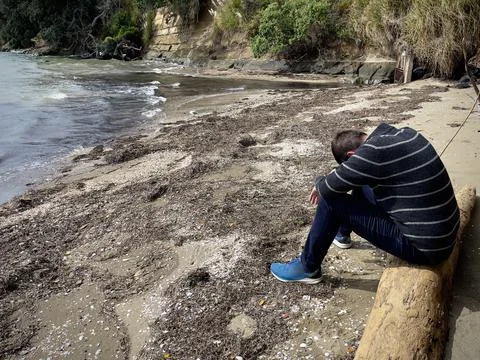 Man sitting on a log at the beach looking upset with his head hanging down betwe Stock Photos