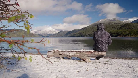 Man Sitting on Log Drinking Yerba Mate by Snowy Lake, Patagonia Stock Footage 327444009