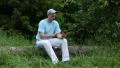Man sitting on log, holding telephone, smiling and adjusted cap HD Footage