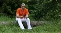 Man sitting on log, holding telephone, earphones, listening music, smiling HD Footage
