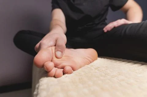 A man sitting on a massage table does self-massage of his feet with his own Stock Photos