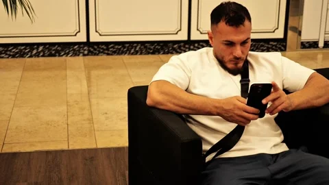Man sitting in modern lobby using smartphone Stock Footage 317849103