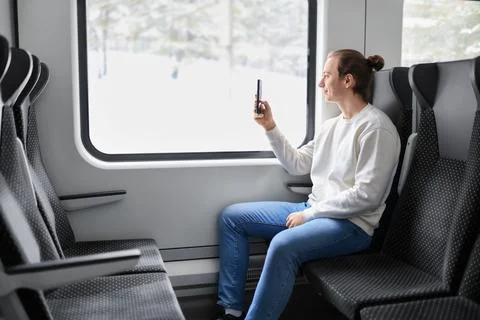 Man sitting in modern train taking photo of winter snowy landscape through .. Stock Photos