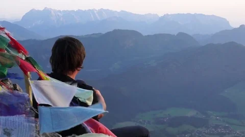Man sitting next to prayer flags and looking at the mountain range Stock Footage