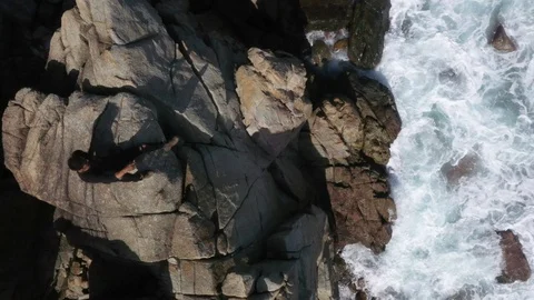 Man Sitting on Ocean Cliff Top Down Aerial Drone Shot Stock Footage 122232841