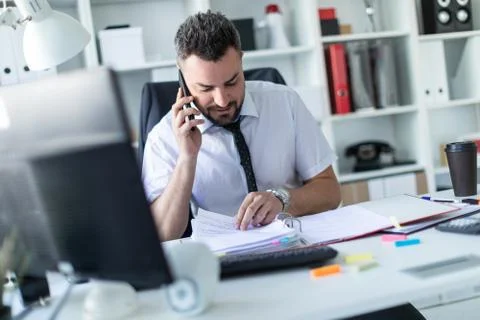 A man is sitting in the office, working with documents and talking on the phone. Stock Photos