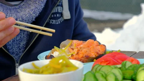 A man is sitting at an outdoor table eating fish and rice using bamboo sticks Stock Footage 170425665