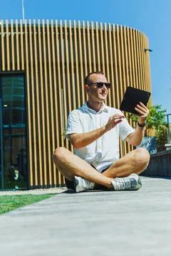 Man sitting outside on path using tablet in front of building with wooden f.. Stock Photos