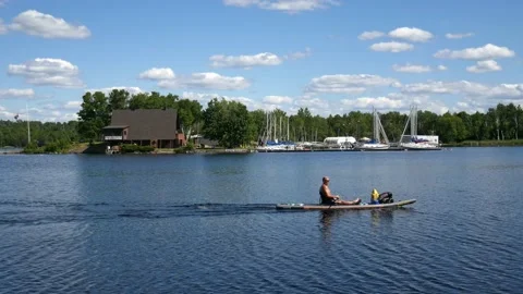 Man sitting on a  paddleboard paddling from left to right on water Stock Footage 200793193