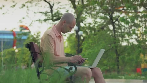A man sitting on a park bench and working with a laptop. Stock Footage 155154872