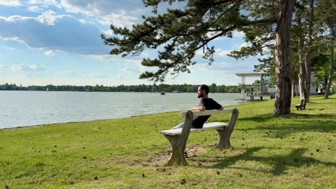 Man Sitting on Park Bench by Scenic Lake Palic Shoreline Vídeos de archivo 336178192