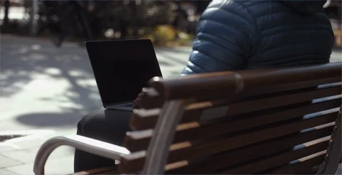 Man sitting at park bench typing on laptop outside Stock Footage 99267924