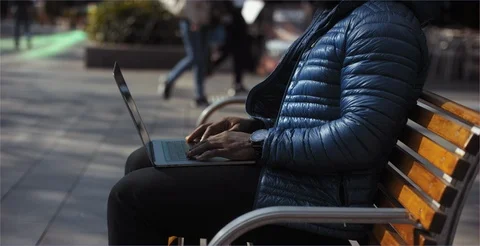 Man sitting at park bench typing on laptop outside closeup Stock Footage 99270943