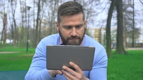 Man sitting in park browsing tablet, looking at camera, close portrait steadycam Vídeos de archivo 74344656