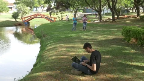 Man sitting in the park by the lake using notebook Stock Footage 70162473