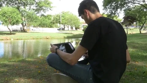 Man sitting in the park by the lake using notebook Video stock 70162527
