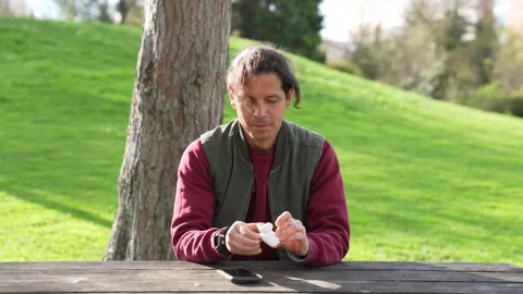 Man sitting in a park spring time listening to music airpods smartphone Stock Footage 237277518