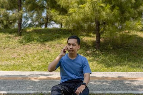 A Man Sitting on Pavement in a Park While Making a Call, Looking Up Thought.. Stock Photos