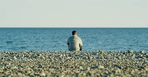 Man sitting at a pebble beach Stock-Footage 77545345
