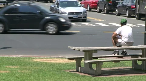 A man sitting on a picnic bench watching traffic. Video stock 8693933