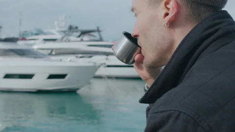 Man sitting on the pier and drinks tea from the thermos cup Stock Footage 151077418