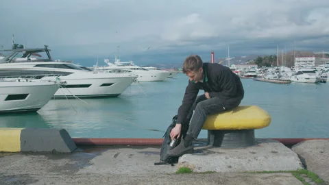 Man sitting on the pier and gets out the thermos Stock Footage 151077305