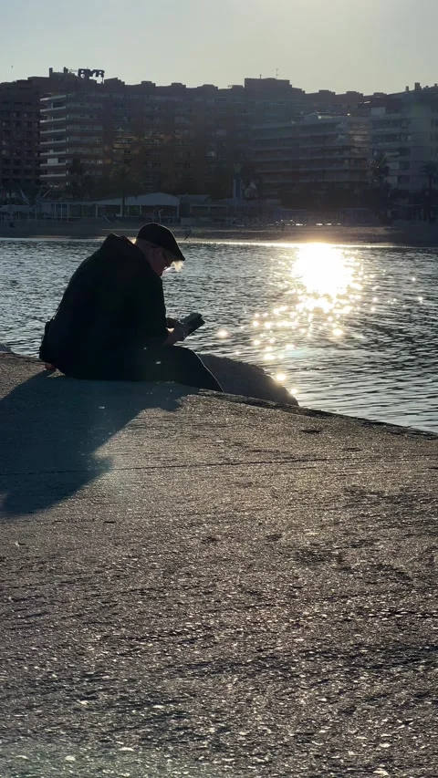 Man sitting on pier and typing in smartphone at sunset in Fuengirola. Vertical Stock Footage 240920729
