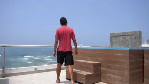 A man sitting by a pool on the terrace of a beach house having a coffee in the Stock Footage 192985348
